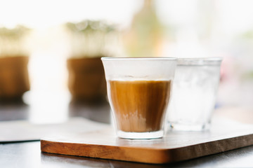 Close up and side view of clear glass of latte coffee with a glass of fresh cold water on beautiful wooden tray.