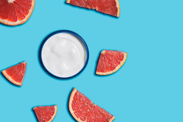 white cream in a jar with grapefruit on blue background. beauty and health care concept. Minimalistic flat lay with copy space. Top view. Cosmetic natural skin care