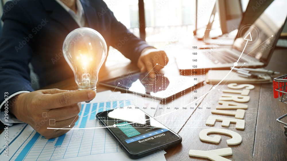 Poster businessman hand holding lightbulb with business documents and strategy word and banking data on sma