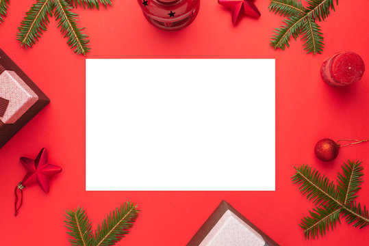 Clean paper for Christmas greeting text suddounded by decorations on red surface. Flat lay, top view composition.