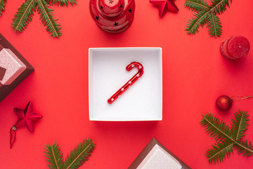 Lollipop in gift box surrounded by Christmas decorations on red surface. Flat lay, top view.