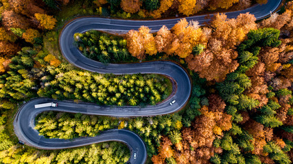 Aerial drone view of winding forest road in the middle of mountains. Colourful landscape with rural road, trees with yellow leaves.