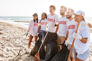 Image of joyful eco volunteers smiling while cleaning beach