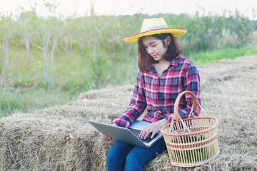 Modern woman farmer sit on straw field farm holding laptop work internet to social media