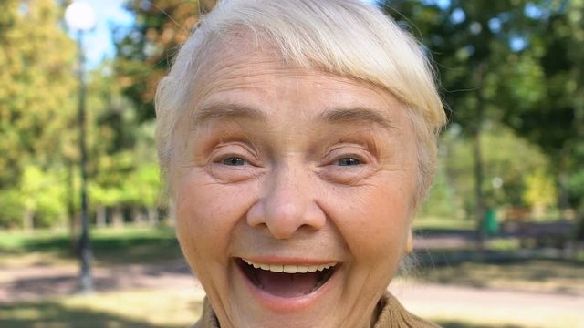 Positive old woman laughing outdoors enjoying good news, surprise happiness
