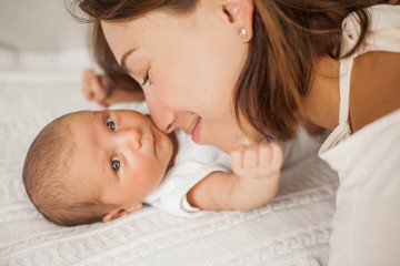 Beautiful young mother plays with the baby in bed. Motherhood.