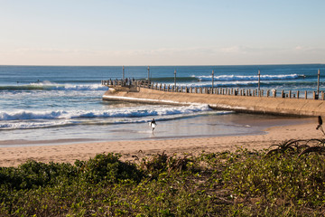 Pier Stretching into Sea with Fishermen and Surfer