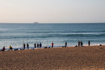 Fototapeta na wymiar Fishermen on the Shoreline with Ship on Horizon