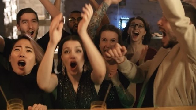 Group of ecstatic young people of different ethnicities watching sports competition at bar, screaming and celebrating success of their favorite team after they winGroup of ecstatic young people of dif