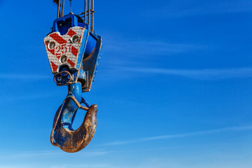 Crane hook with red and white stripes hanging, blue sky with white clouds background, detail