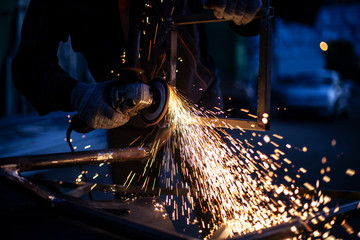 Sparks from metal sawing. A man is cutting a metal profile with a grinder. Work in the garage. Creation of construction. Sparks from heating. The disc rotates and cuts metal.