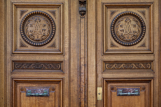 Old wooden door. Gorgeous ornate natural wood door panels with elegant monogram ornaments and antique handles. Details of Paris door of ancient building in France. Classical architectural features