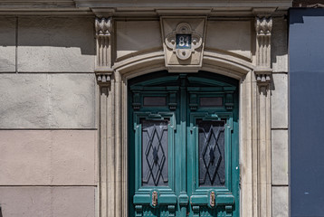 Facade of old house with classical architecture sculptural arch doorway and green painted wooden door with rhombus pattern grids on door windows. Details of Paris door of stone building in France.
