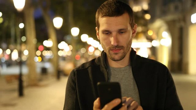 Front view portrait of a serious and happy adult man checking mobile phone walking in the 