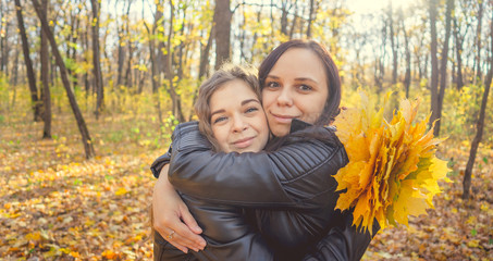 Two young women are hugging on a walk in the autumn forest. Girlfriends met to walk in a warm weather.
