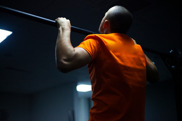 A man is training. The guy pulls himself up on the horizontal bar. A strong man pumps his muscles. Classes in the gym. Work on the body. White guy shakes his biceps.