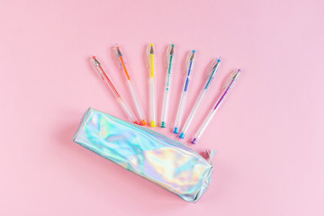 Gel pens of rainbow colors and a pearl pencil case on a pink background. Place for text,...