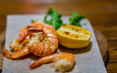 fried roasted shrimps with lemon and arugula on wooden table