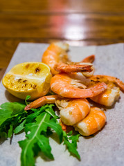 fried roasted shrimps with lemon and arugula on wooden table