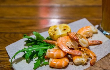 fried roasted shrimps with lemon and arugula on wooden table