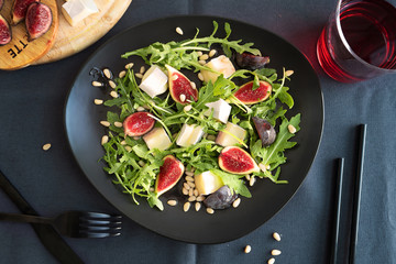 CAMEMBERT AND FIG SALAD on black plate in dark grey tablecloth.