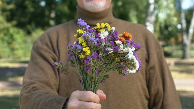 Senior male pensioner stretching out hand with wildflowers, date present, love