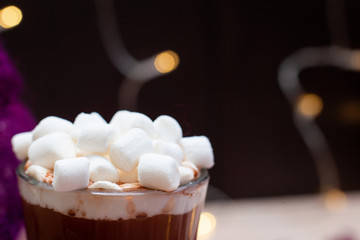 Hot Cocoa with marshmallows close-up in a transparent glass on a background of bokeh from New Year lights.