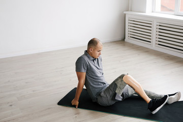 Young man with prosthetic leg sitting on exercise mat and resting after sports training