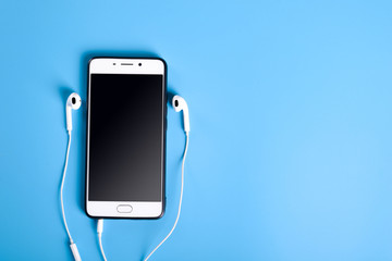  Mobile headphones and a mobile phone of white color on a blue background in light colors with a place for text.