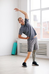 Young disabled man standing raising his arm and stretching during sports exercises