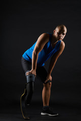 Fototapeta na wymiar Portrait of young paralympic sportsman with leg prosthesis looking at camera isolated on black background