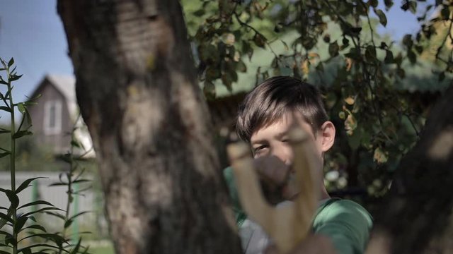 funny boy hides behind a tree and aims with a slingshot outdoors