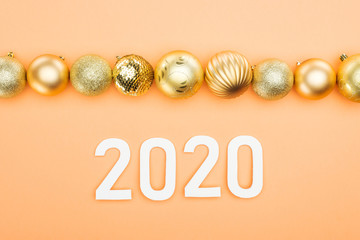 top view of white 2020 numbers near golden christmas baubles on orange background