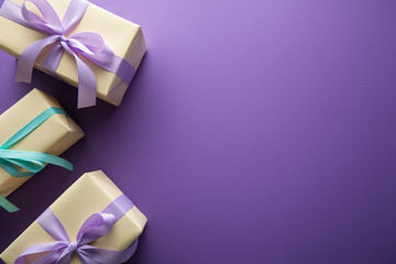 top view of gift boxes with colorful ribbons and bows on purple background with copy space