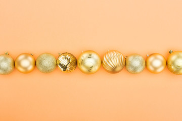 top view of golden christmas baubles in row on orange background