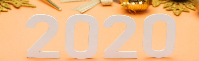 white 2020 numbers near golden christmas decoration on orange background, panoramic shot