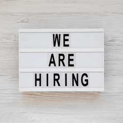 'We are hiring' words on a modern board on a white wooden background, view from above. Top view, overhead, flat lay. Closeup.