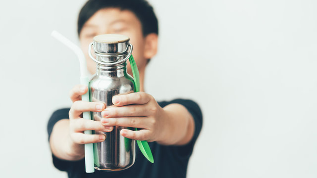 Eco-friendly lifestyle concept. Cool teenage Asian boy look, stretch his arms forward holding reusable stainless bottle, green spoon and fork, and silicone straw to campaign Stop Single Use Plastic.