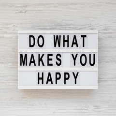 'Do what makes you happy' words on a lightbox on a white wooden surface, top view. Overhead, from above, flat lay.