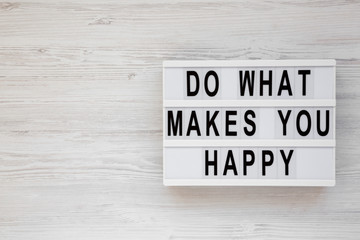 'Do what makes you happy' words on a lightbox on a white wooden background, top view. Overhead, from above, flat lay. Copy space.