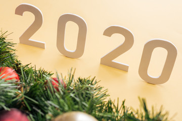 paper 2020 numbers near Christmas tree branch with baubles on yellow background