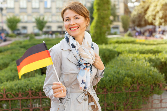 Happy middle aged woman with the German flag on a background of the park and the city.