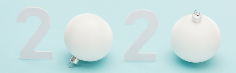 white 2020 numbers near Christmas baubles on light blue background, panoramic shot