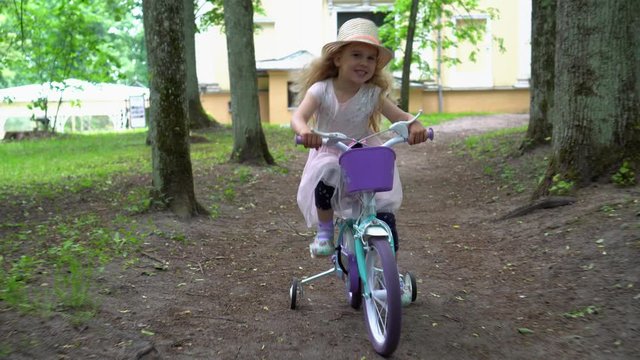 Elegant female child model in pink dress ride bike on four wheels. Gimbal shot