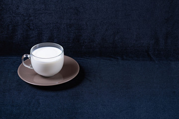 Glass mug with milk on saucer and dark cloth background