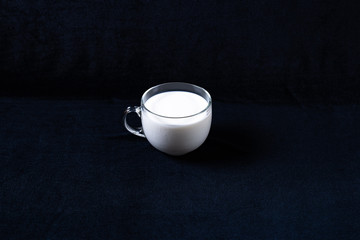 Glass mug with milk on dark fabric background
