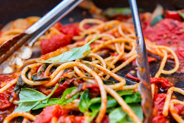 A pan of rustic cooked spaghetti / pasta, sweet tomato sauce and basil leaves.