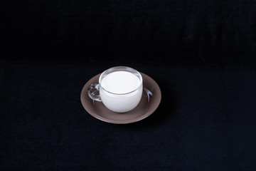 Glass mug with milk on saucer and dark cloth background