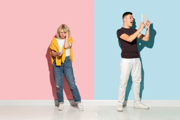 Young emotional man and woman in bright casual clothes posing on pink and blue background. Concept of human emotions, facial expession, relations, ad. Woman's sad, man's astonished, crazy happy.