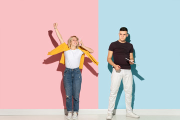 Fototapeta premium Young emotional man and woman in bright casual clothes posing on pink and blue background. Concept of human emotions, facial expession, relations, ad. Man's sad, woman's astonished, crazy happy.
